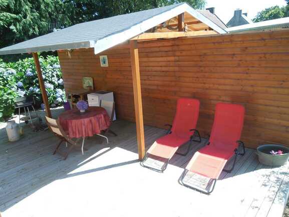 Une terrasse en bois privative semi-couverte avec salon de jardin et barbecue